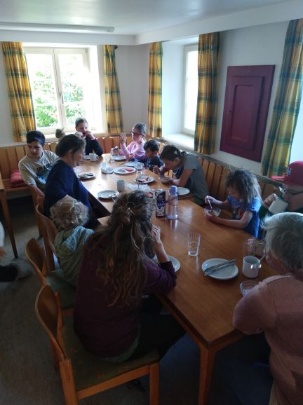 Etwa 10 Menschen unterschiedlichen Alters sitzen um einen Tisch und essen